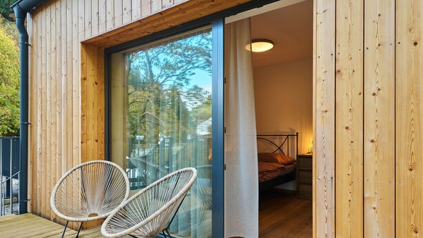 A wooden cabin with a sliding glass door leading to a bedroom with a bed and a nightstand.