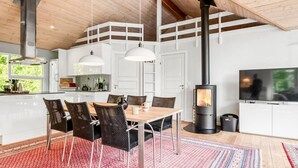Una cocina moderna con armarios blancos, una zona de comedor con sillas de mimbre y un estufa de leña.