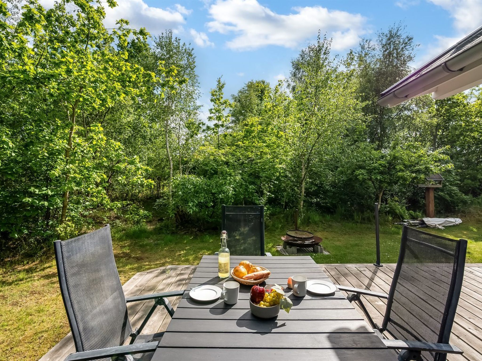 An outdoor dining area with a table set for two, surrounded by lush greenery.