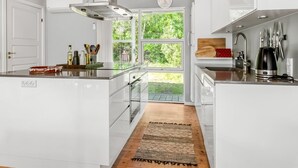Cocina moderna con gabinetes blancos, extractor de acero inoxidable y un amplio ventanal con vistas a la vegetación.