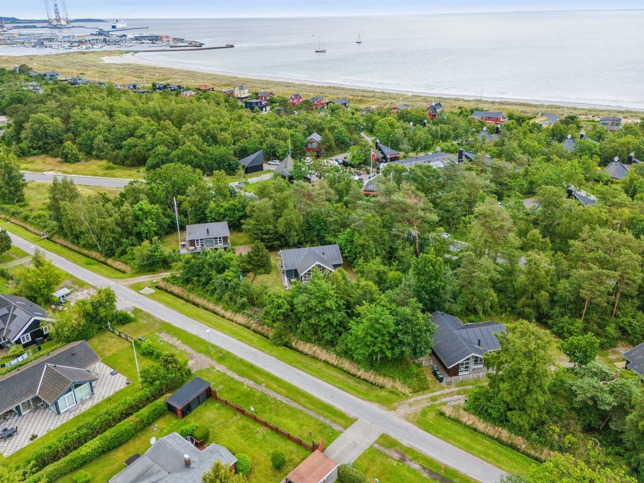 Vue aérienne d’un quartier résidentiel avec des maisons, des routes et une étendue d’eau en arrière-plan.