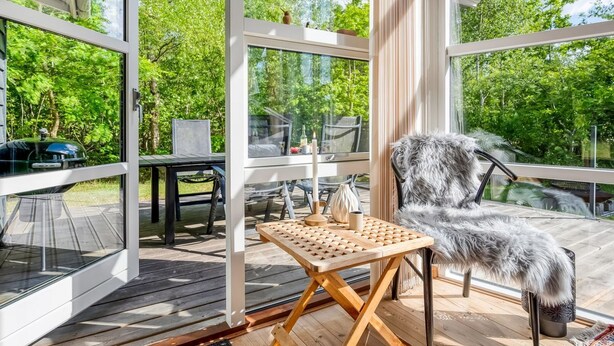 Una terraza moderna al aire libre con paredes de vidrio, una mesa de madera y un sillón mullido.