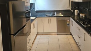 A modern kitchen with stainless steel appliances, light-colored cabinets, and a black countertop. - Mornington peninsula getaway (Frankston)