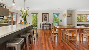 A modern kitchen with a bar area, wooden flooring, and large windows offering views of greenery.