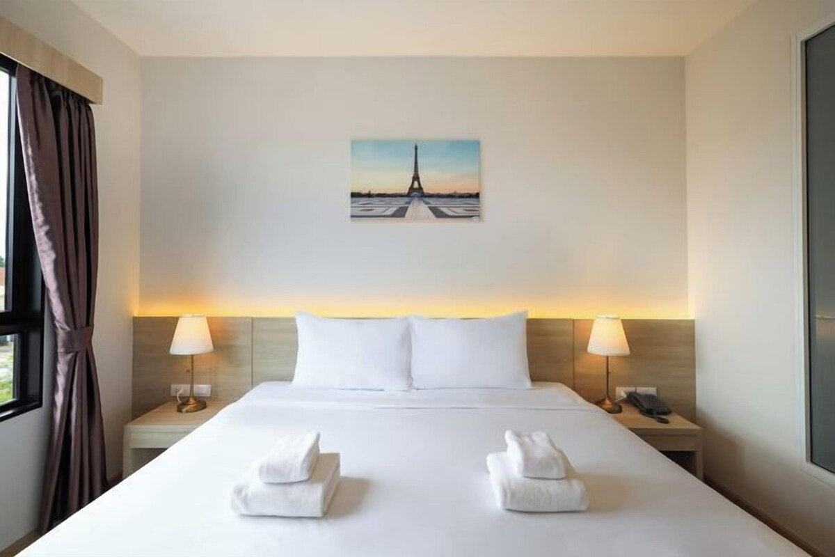Habitación de hotel con una cama grande, dos lámparas de noche, un cuadro de la Torre Eiffel y una ventana con cortinas.
