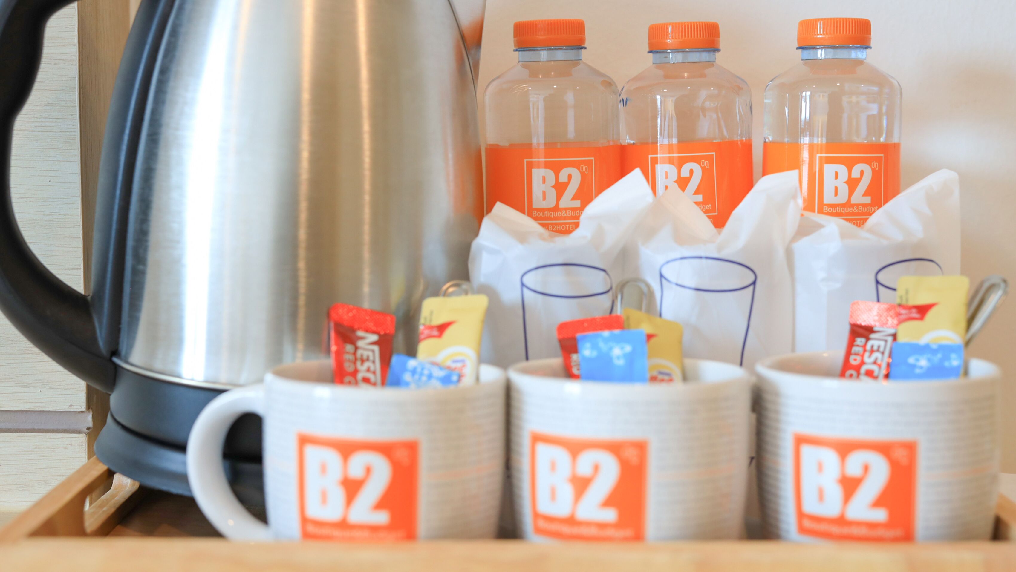 A kitchenette area with a kettle, four B2 branded bottles, and various food items in cups.
