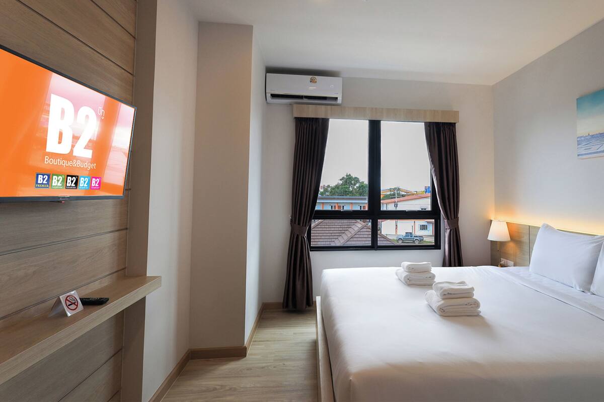 Ein Hotelzimmer mit einem Bett, einem Fernseher, einem Fenster mit Vorhängen, einem Bildstempel des Eiffelturms und einer Klimaanlage.