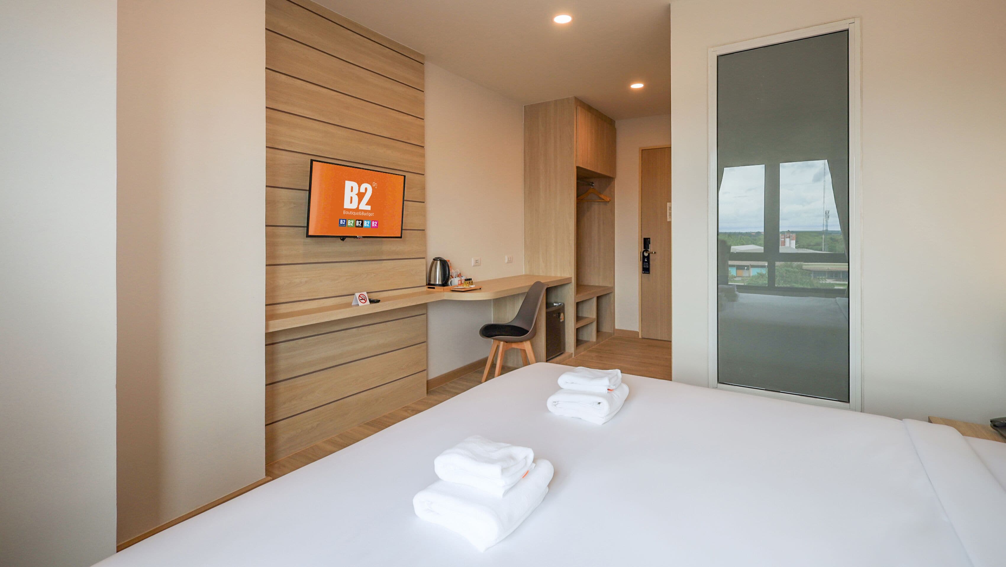 Une chambre d’hôtel moderne équipée d’un lit, d’un bureau, d’une chaise, d’un téléviseur fixé au mur et offrant une vue sur l’extérieur grâce à une porte vitrée.