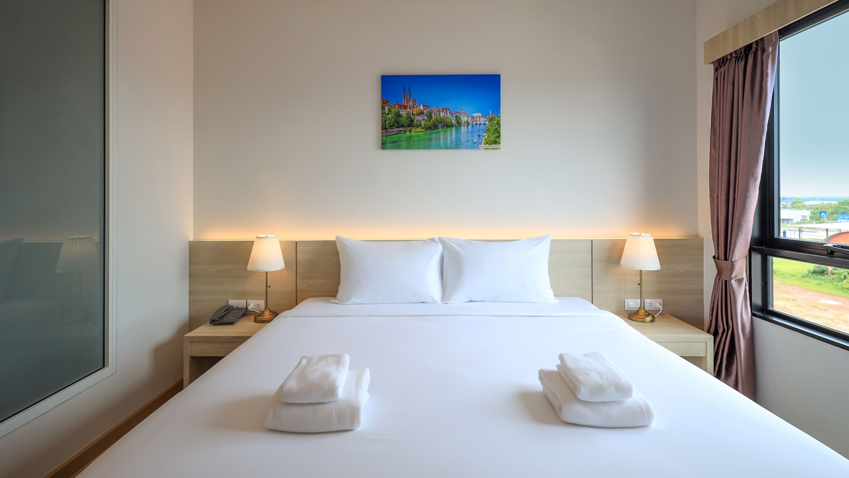 Une chambre d’hôtel avec un grand lit, deux tables de chevet, un tableau représentant un paysage urbain et une vue par la fenêtre.