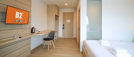 Habitación de hotel con cama, escritorio, silla, televisor montado en la pared y puerta que da al pasillo.