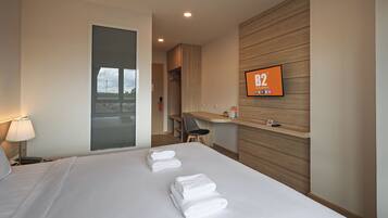 A hotel room with a bed, a desk, a chair, a TV, and a view of the outside.