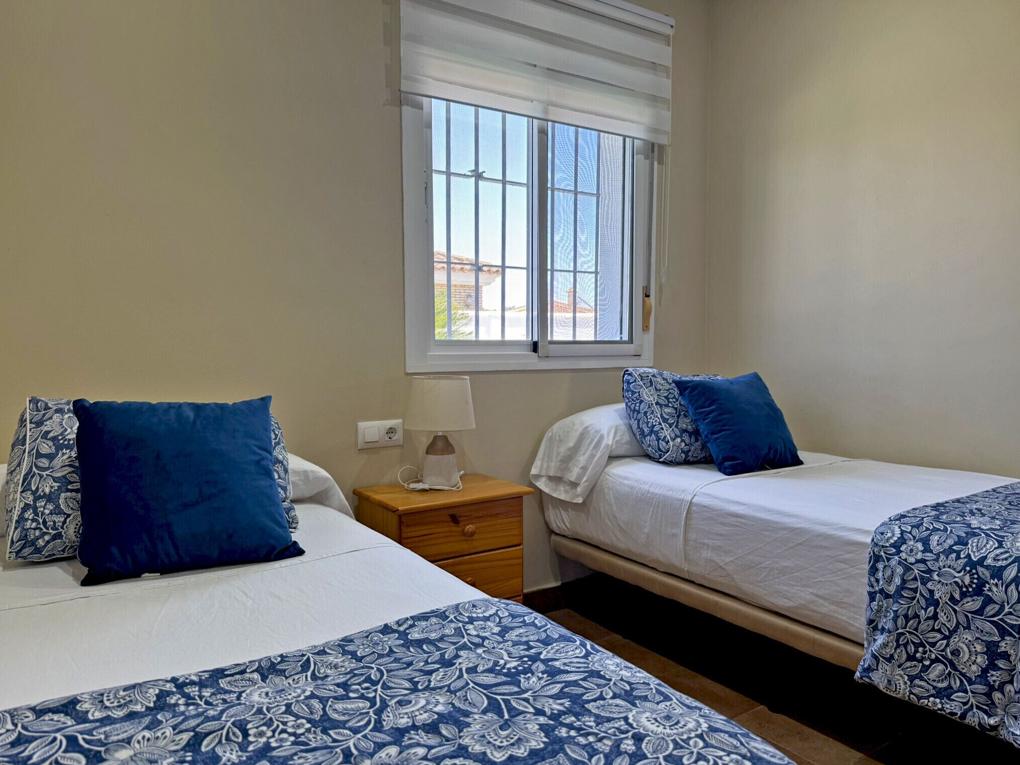 A bedroom with two beds, a nightstand, a lamp, and a window with blinds.