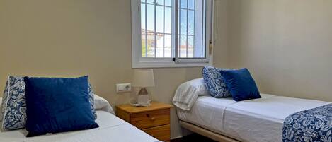 A bedroom with two beds, a nightstand, a lamp, and a window with blinds.