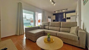 Un salón moderno con un sofá modular, una mesa de centro redonda con una planta y vistas al patio trasero a través de grandes puertas correderas de vidrio.
