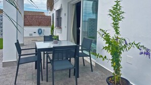 Un patio con una mesa y sillas de vidrio, un colgante de luz y una planta en maceta.