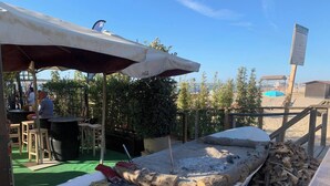 A boat with 'EL INESCUERTO' written on it, docked at a beachside bar area with outdoor seating and a Coca-Cola branded umbrella. - Apartamento Alborada - Ole Solutions (Sanlúcar de Barrameda)