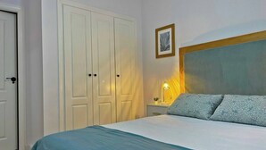 A bedroom with a bed, a nightstand, a lamp, and a wardrobe. - Apartamento Alborada - Ole Solutions (Sanlúcar de Barrameda)