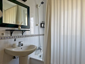 Un bany amb un lavabo, mirall, dutxa i cortina rayada.