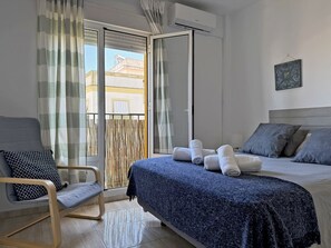 A hotel room with a bed, a chair, a balcony with curtains, and an air conditioning unit.