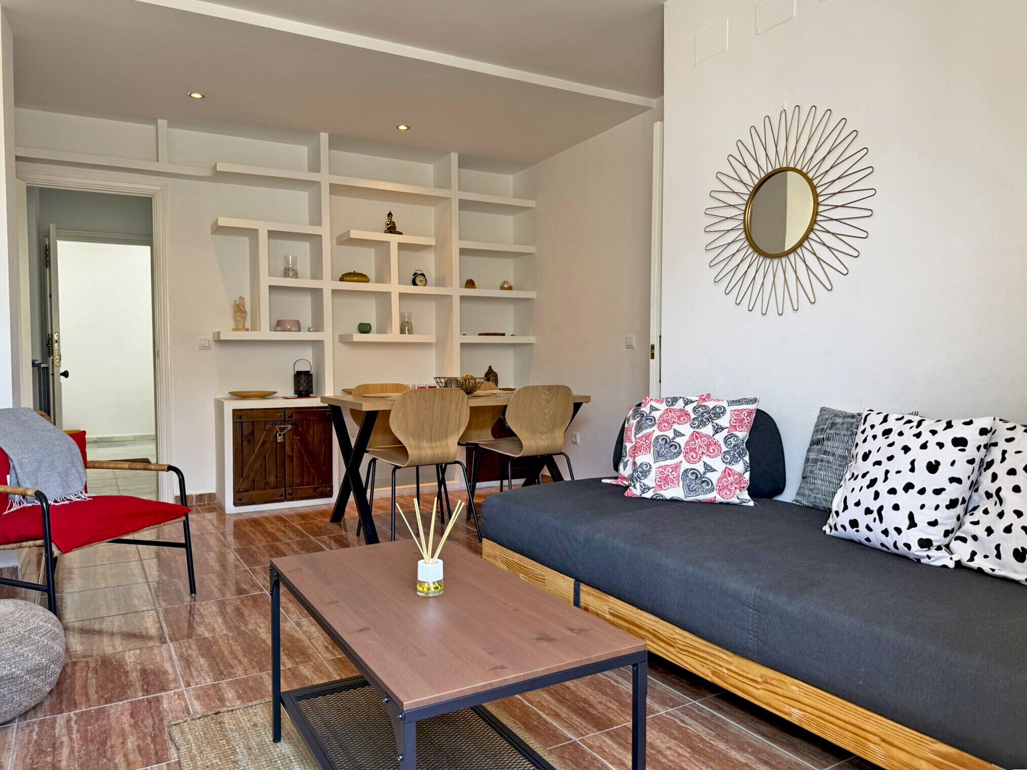 A living room with a sofa, a coffee table, and a dining area with chairs and shelves.
