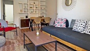 A living room with a sofa, a coffee table, and a dining area with chairs and shelves. - Apartamento La Paquera - Ole Solutions (Jerez de la Frontera)