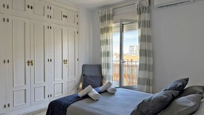 A bedroom with a bed, a chair, a wardrobe, and a view through a window. - Apartamento La Paquera - Ole Solutions (Jerez de la Frontera)
