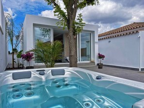 Un espace moderne aménagé à l’extérieur, avec un jacuzzi, offrant une vue dégagée sur une maison contemporaine en arrière-plan.