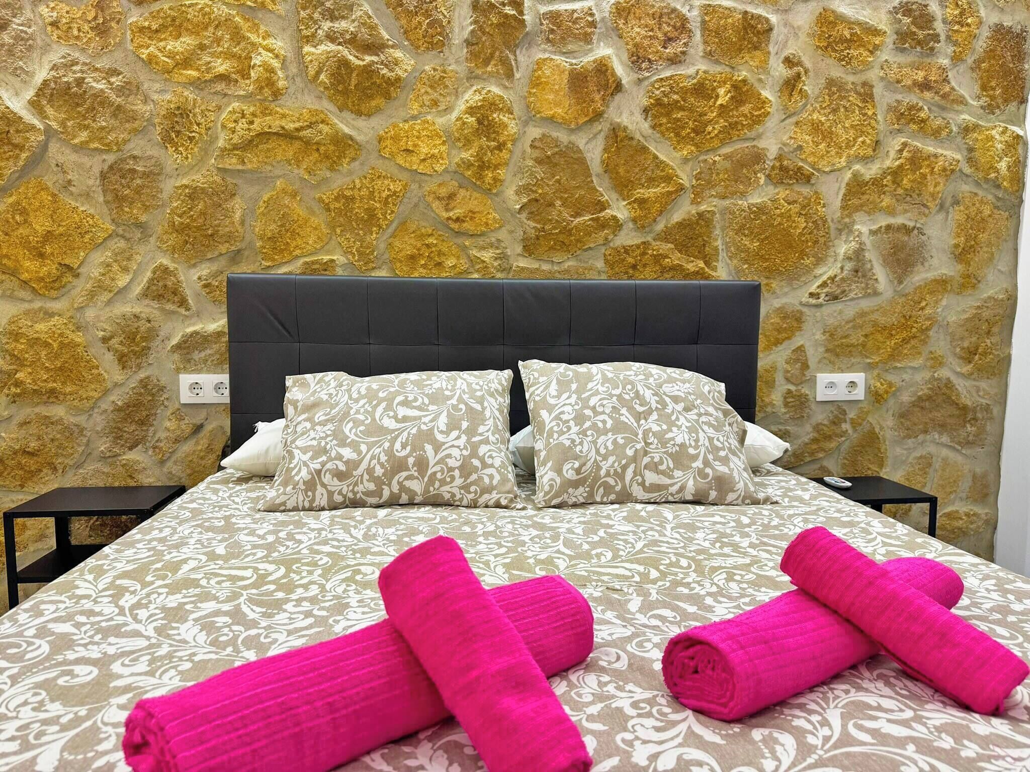 Een bed met een beddeken met patroon, twee kussens en twee opgerolde handdoeken.