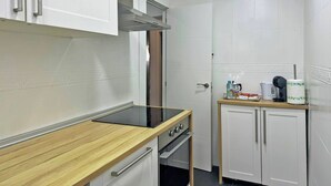 A compact kitchen with white cabinets, a wooden countertop, a built-in oven, and a coffee maker on a small table.