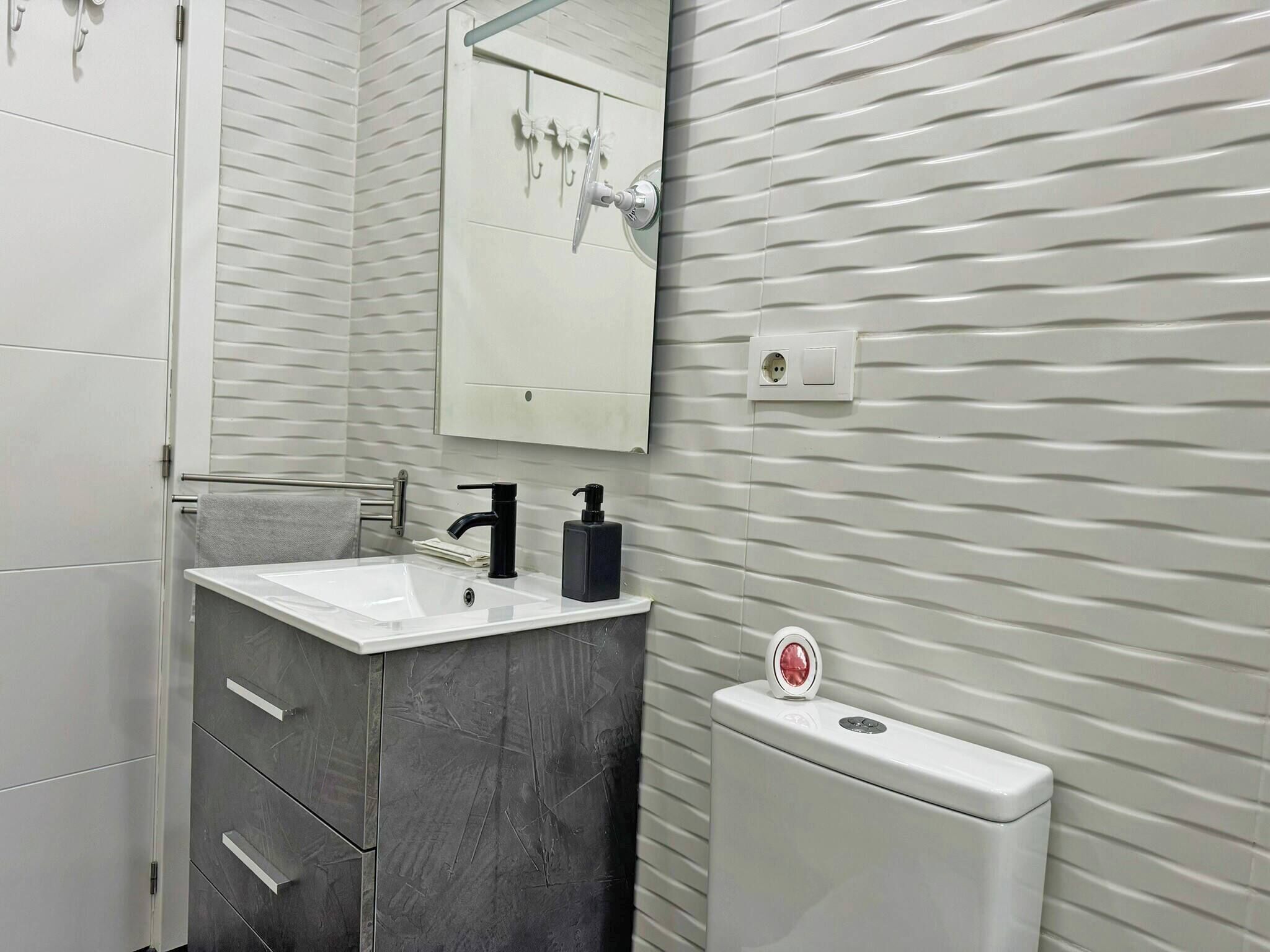 A modern bathroom with a white sink, black faucet, and a toilet with a flush button.