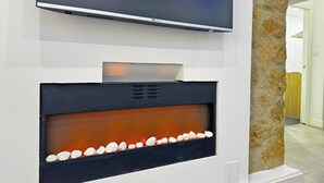 A modern fireplace with a TV above it, set against a stone wall.
