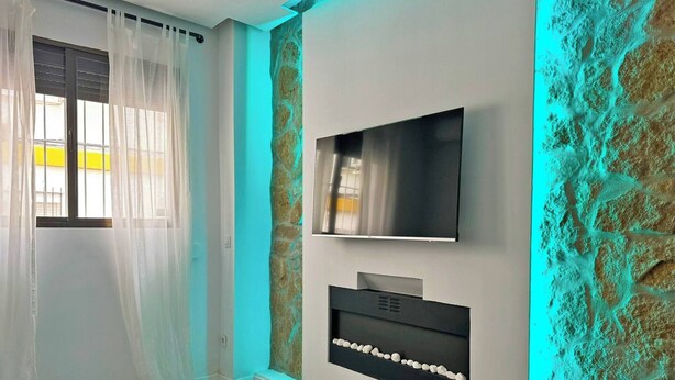 A modern living room with a flat-screen TV mounted on the wall, a built-in fireplace, and a stone-textured accent wall.
