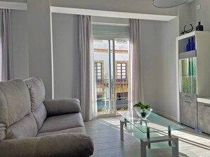A modern living room with a grey sofa, a glass coffee table, and a view of a balcony with a railing.