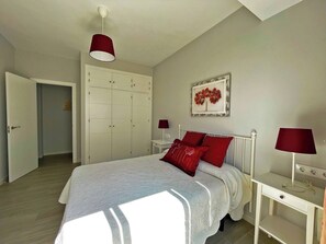 A bedroom with a bed, a wardrobe, a bedside table, a lamp, and a wall art piece.
