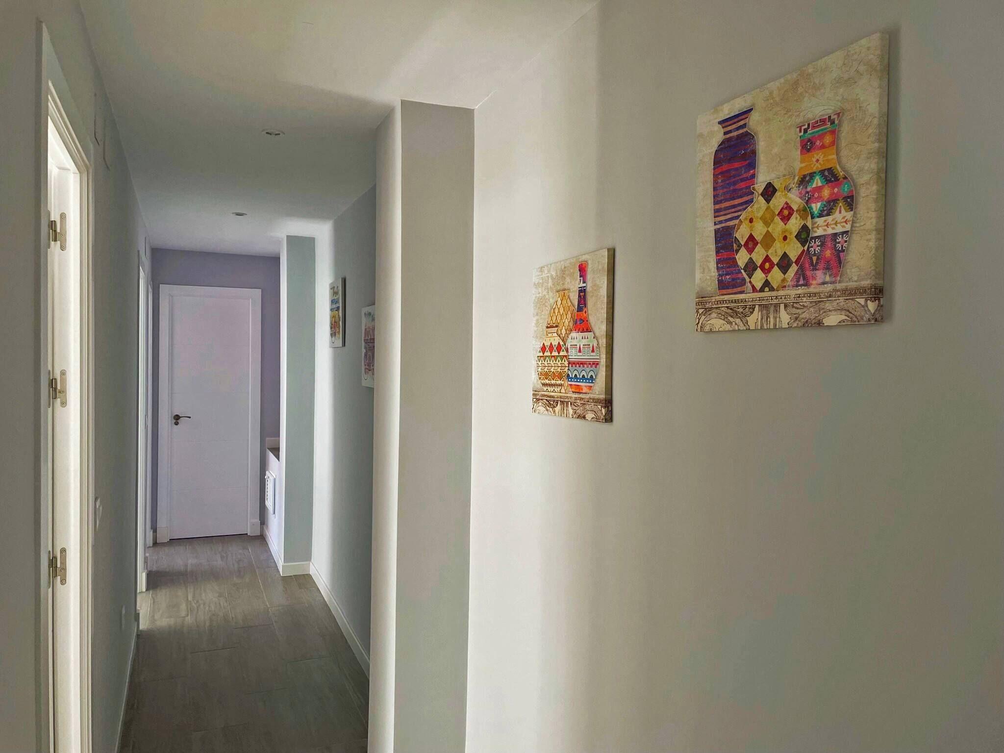 A hallway with a door at the end, two artworks on the wall, and a light switch.