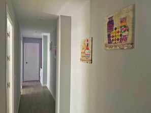 A hallway with a door at the end, two artworks on the wall, and a light switch.