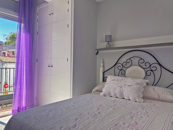 A bedroom with a bed, a headboard, a nightstand, and a window with purple curtains.