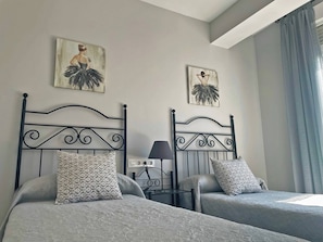 Habitación de hotel con dos camas, cada una con almohadas y cabeceros estampados. Se observan obras de arte colgadas en la pared sobre las camas y una mesita de noche con una lámpara.
