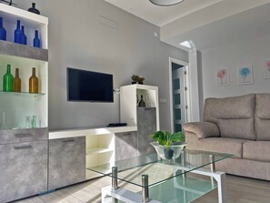 A modern living room with a glass coffee table, a beige sofa, and a TV mounted on the wall. - Apartamento La Catedral - Ole Solutions (Jerez de la Frontera)