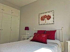 Ein Schlafzimmer mit Bett, Nachttisch, Lampe, Kleiderschrank und einem gerahmten Bild an der Wand.