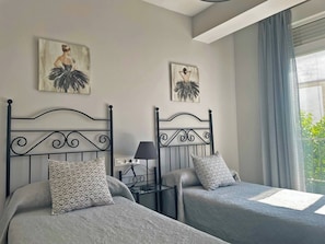 A hotel room with two beds, a nightstand, a lamp, and artwork on the walls.