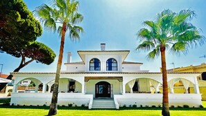 Une maison à deux étages avec une piscine à l’avant, entourée de palmiers et d’une pelouse bien entretenue.