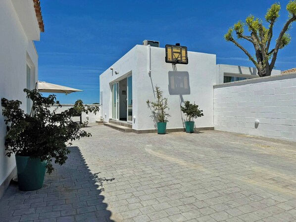 A courtyard with a white building, potted plants, and a basketball hoop.
