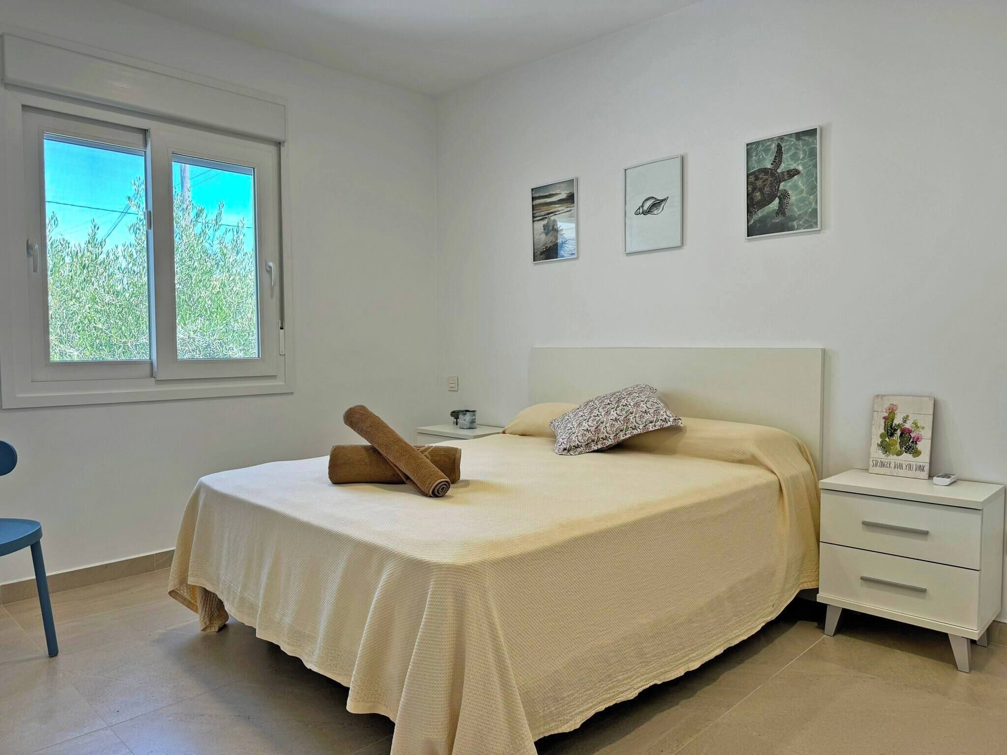 A bedroom with a bed, a nightstand, a chair, and a window with a view of greenery.