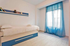 Une chambre à coucher avec un lit, une étagère remplie de livres et un rideau bleu transparent.