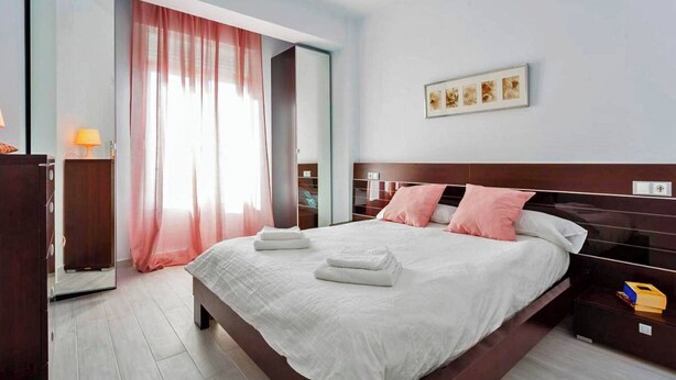 Quarto de hotel moderno com uma cama grande, um guarda-roupa, uma mesa de cabeceira e uma janela com cortinas.
