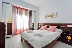 Ein modernes Hotelzimmer mit einem großen Bett, einem Kleiderschrank, einem Nachttisch und einem Fenster mit Vorhängen.