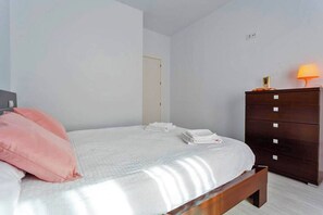 Un dormitorio con cama, almohadas, cómoda y lámpara.