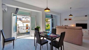 Uma sala de estar moderna com um sofá, uma mesa de jantar com cadeiras, luminárias pendentes e uma TV na parede.