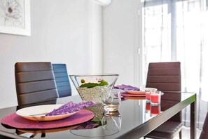 Ein Esstisch mit einer transparenten Glasdekoration, violetten Platzsets und einem Glas Wasser.
